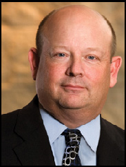 Portrait of Benjamin Novosad in a black suit and tie against a beige backdrop