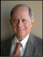 Brian Weiner smiling in a grey suit and red tie in front of a beige background