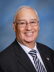 Britt Jarvis smiling in a black suit and striped tie in front of a blue backdrop.