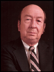 C. G. Scruggs in a black suit and striped yellow tie against a black backdrop.