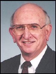 Delmar Deterling smiling in a black suit in front of a gradient blue background.