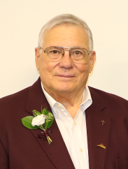 Ernest Davis smiling in a maroon suit with a white flower pinned to the lapel in front of a cream backdrop.