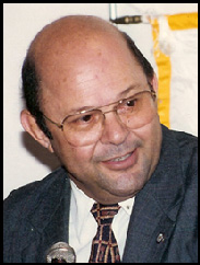 Portrait of Fernando Quinonez-Meza smiling in a black suit in front of a microphone.