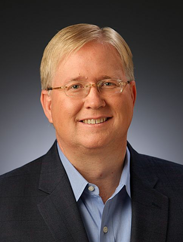 Graham Weston smiling in a black suit against a gradient background