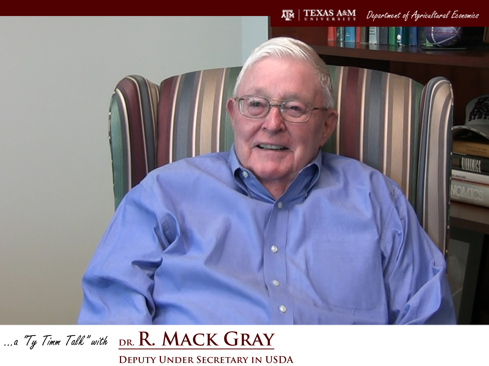 The words "a ty timm talk with Dr. R. Mack Gray - Deputy under Secretary in USDA" run along the bottom. Mr. Catalena is seated in a striped, high-backed chair and wearing a blue button-up, smiling. in front of a bookcase.