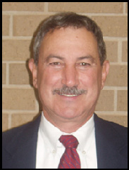 Jimmy Roppolo smiling in a black suit and red tie in front of a brick wall.