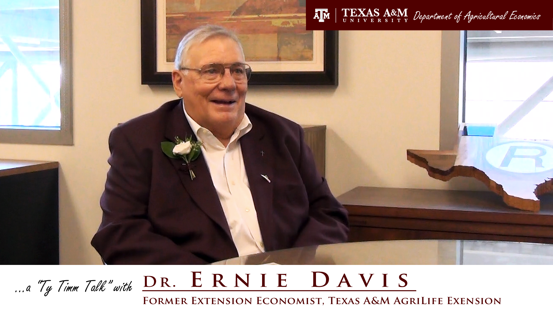 The words "a ty timm talk with Dr. Ernie Davis - Former Extension Economist, Texas A&M AgriLife Extension" run along the bottom. Dr. Davis, in a black suit and white flower pinned to suit jacket, is seated at a table.