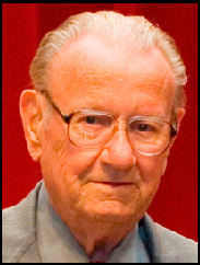 Jesse Grady smiling in a grey suit against a red backdrop.