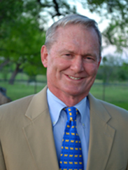 Jim McAdams smiling in a tan suit and blue tie in an outdoor setting