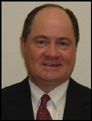 John Windwehen smiling in a black suit and red tie against a white backdrop