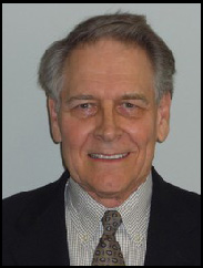 Jon Hagler smiling in a black suit in front of a white background.