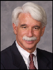 Jorge Bermudez in a black suit and red tie, smiling against a grey background.