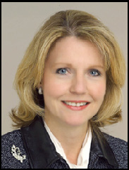 Kathleen Gibson smiling in a black suit against a beige backdrop