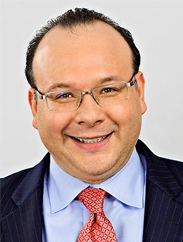 Ken Hogan smiling in a dark suit and red tie against a white backdrop