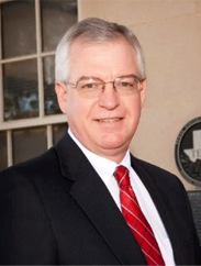 Ken Leiber smiling in a black suit and red tie in front of a window.