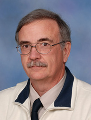 Larry Falconer in a white jacket and black tie against a blue background.