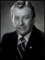 Robert Kensing in black and white, wearing a suit and smiling