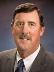 Russell Boening smiling in a dark grey suit against a dark blue background