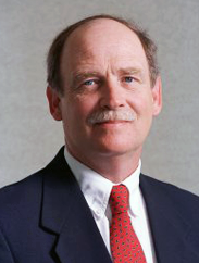 Stephen H. Amosson in a dark blue suit, white shirt, and red patterned tie, smiling.