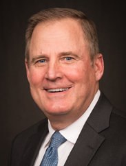 Steve LaMantia smiling in a black suit and blue tie against a black backdrop