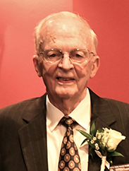 Jimmie Holder smiling in a black suit against a red background.