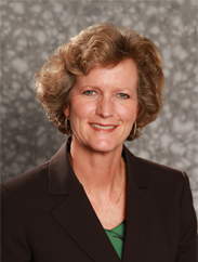 Lisa Tanner smiling in a black suit and green dress shirt in front of a grey backdrop