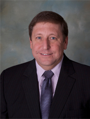 Mark Patranella smiling in a black suit and purple tie in front of a grey backdrop