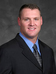 Robert Goodwin smiling in a black suit and tie against a dark grey backdrop.