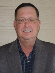 Larry Kokel smiling in a dark grey suit against a wooden cream background.