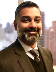 Christopher Narayanan smiling in a grey suit against a skyline.