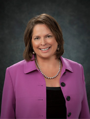 Mary Ledmen smiling in a purple coat and black top against a black backdrop