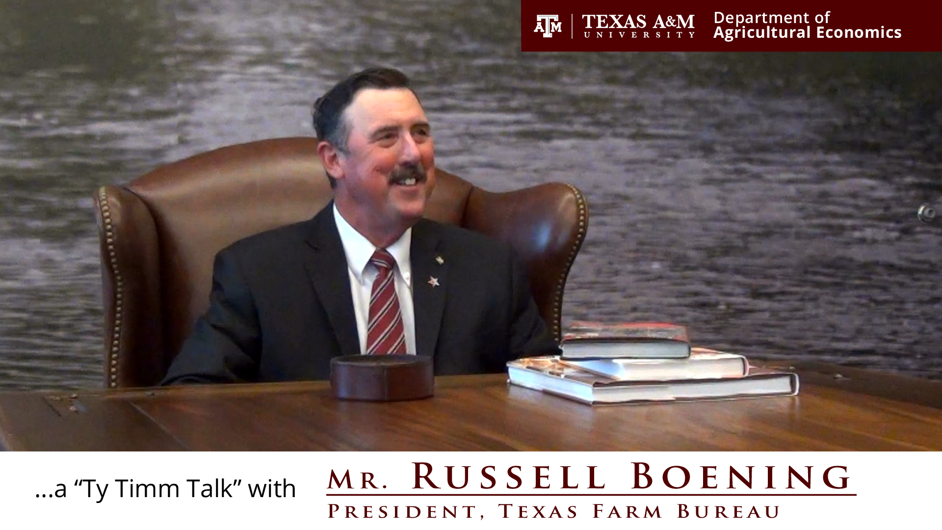 The words "a ty timm talk with Mr. Russell Boening - president, Texas Farm Bureau" run along the bottom. Mr. Boening, smiling, is seated in a dark brown leather chair at a brown, chest high table in a black suit. 